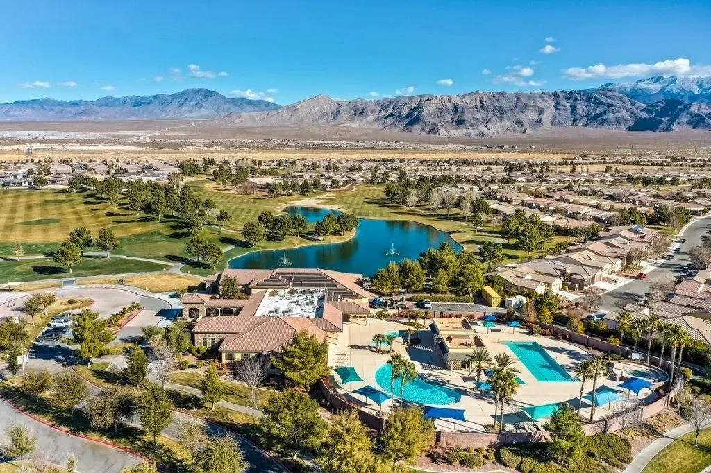 Aerial view of a resort-style pool, clubhouse and golf course lake, with the mountains beyond