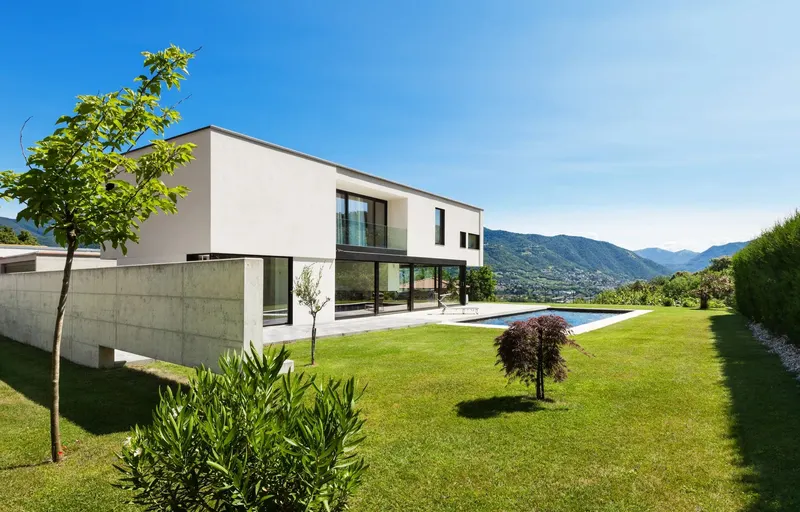 A modern white house with a lawn and pool, hills behind