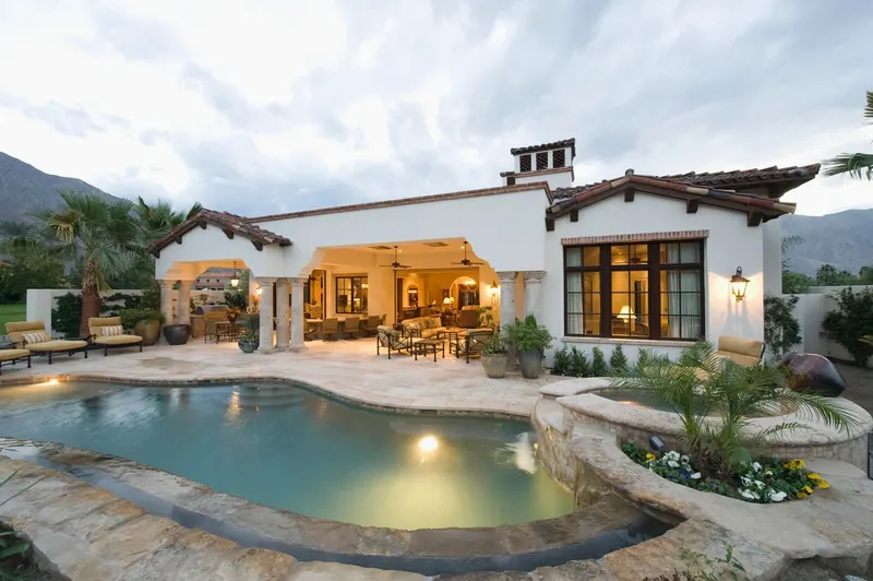 A white stucco house with a lit pool and patio at dusk