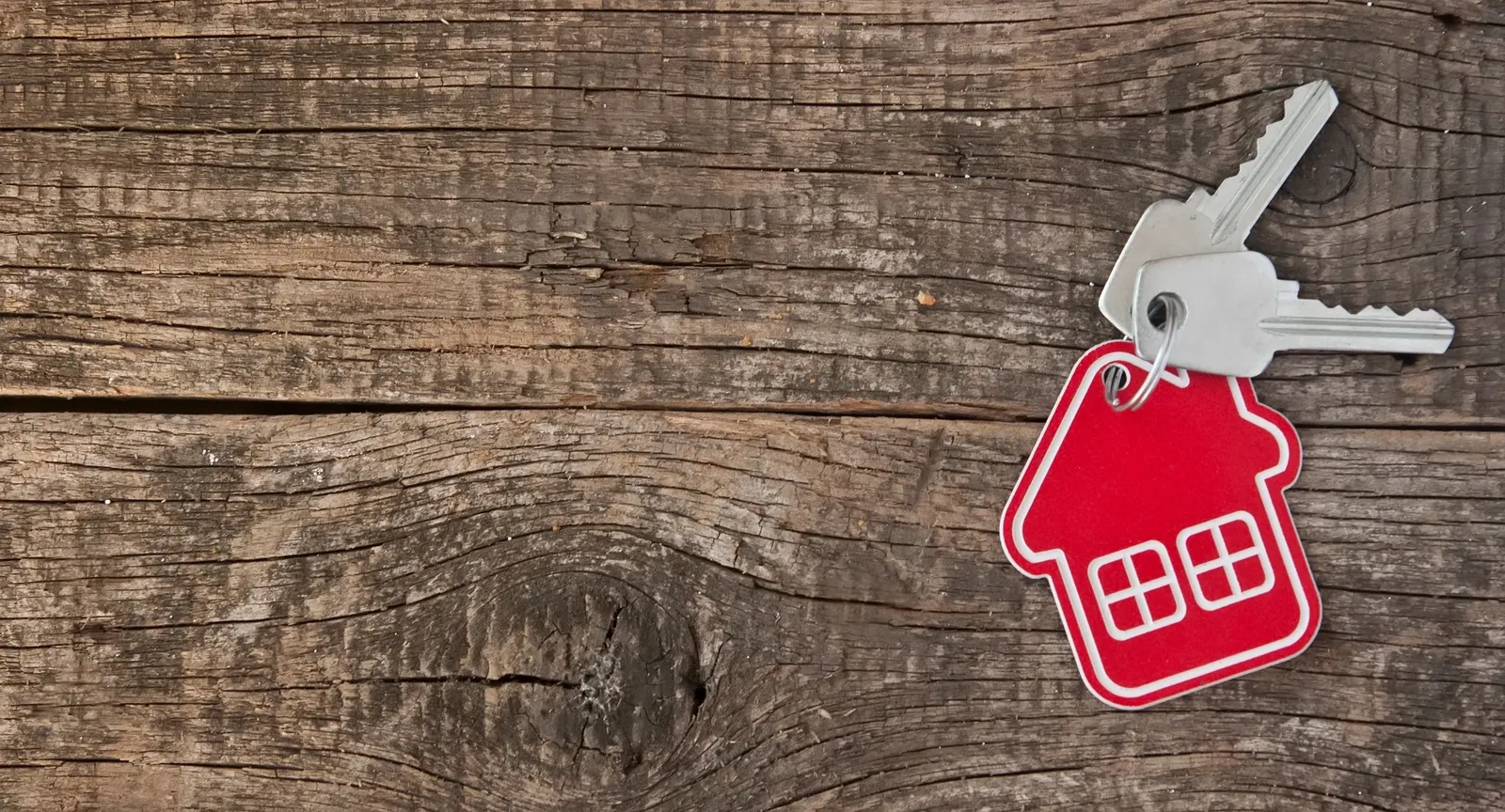 House keys on a red house-shaped key ring, on weathered wood